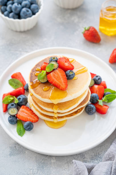 istock A stack of delicious fluffy pancakes with berries and honey on a white plate on a gray concrete background. Copy space. 1386866770