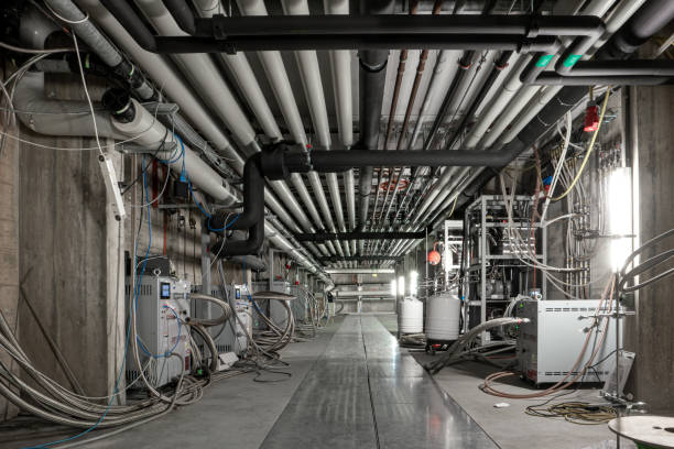 Ceiling mounted industrial pipelines and science laboratory machinery inside underground building, Long corridor with metal floors, dimly lit, no people stock photo