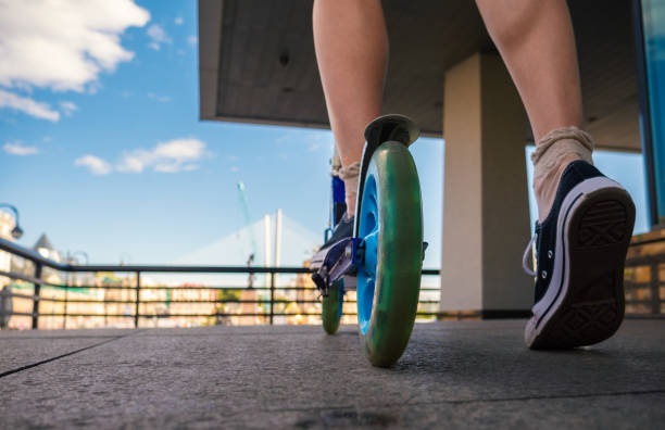 Legs of young woman on kick scooter at street.