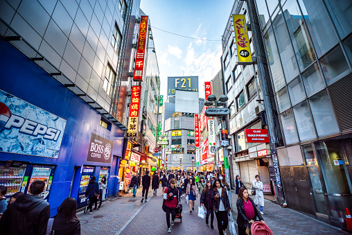 View of Shibuya shopping street with people and neon signs during sunset
