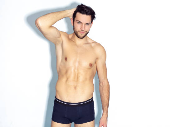 Athletic And Strong Handsome Caucasian Man Wearing Contrasty Underware Outfit And Posing With Lifted Hand Over White Background. Horizontal Image Composition