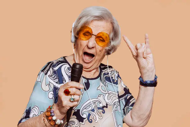 Photo of Funny elderly rockstar grandmother singing karaoke with microphone at studio