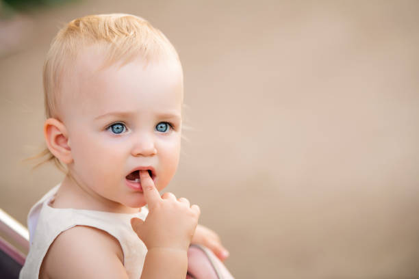 retrato de un bebé de ojos azules chupando el dedo en la boca, dos primeros dientes son visibles. - ojos azules fotografías e imágenes de stock