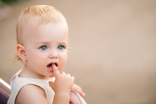 Portrait of a blue-eyed baby sucking a finger in her mouth, two first teeth are visible.