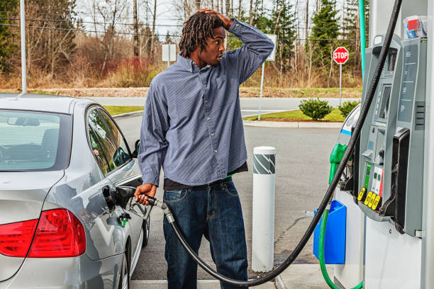 Young Man at Gas Station in Shock Over Sale Price Photo of a young African American man at a gas station, filling his tank with a look of shock as he looks at the sale price car gas pump stock pictures, royalty-free photos & images