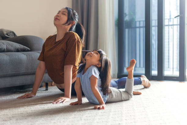 mother and young daughter practicing cobra yoga pose at home. stock photo