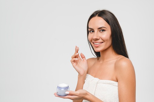 Closeup caucasian beautiful young woman with clean skin applying cosmetics for dermatology care, anti-acne anti-age effect, hydration and moisturizing isolated in grey background.