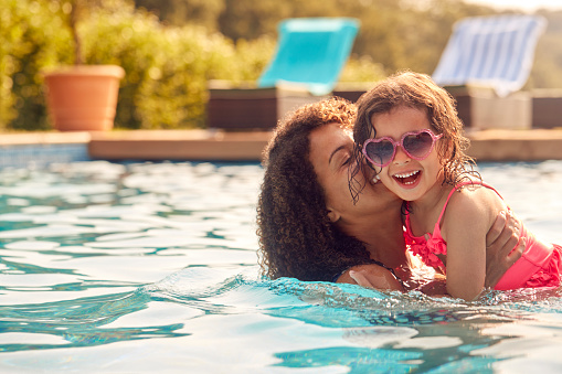 Madre e hija riendo con gafas de sol divirtiéndose en la piscina en las vacaciones de verano photo