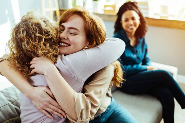 Women relax together in group therapy Caring female counselor hugs a female patient during a group therapy session. mercy hug stock pictures, royalty-free photos & images