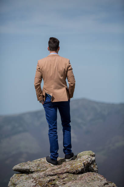 Back view of elegant young man standing on the top of the mountain
