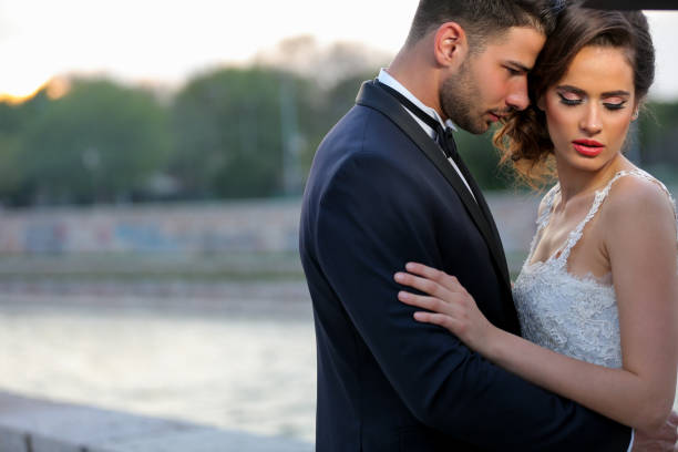 Portrait of young newlywed couple standing and hugging by the river on sunny day
