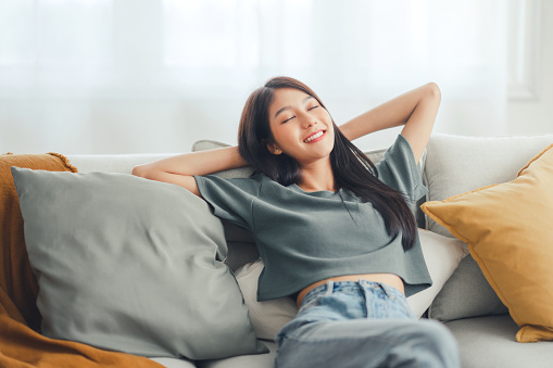 Closeup - Relaxed young asian woman enjoying rest on comfortable sofa at home, calm attractive girl relaxing and breathing fresh air in home, copy space.