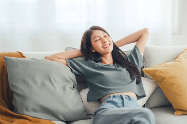 Relaxed young asian woman enjoying rest on comfortable sofa at home, calm attractive girl relaxing and breathing fresh air in home stock photo