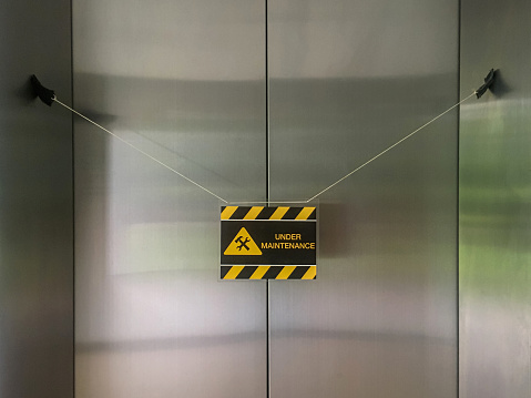 Frontview shot of a closed elevator with a warning sign hanging across the door frame to tell people that the elevator is currently under maintenance.