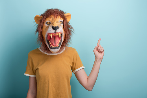 Woman in lion mask pointing with hand and index finger to the side blank space, isolated on blue background