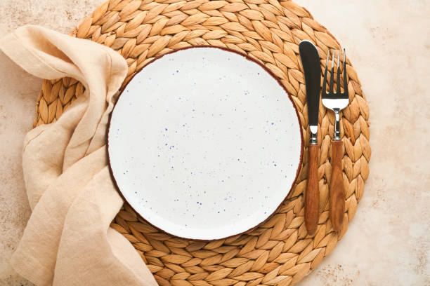 istock Vintage zero waste silverware. Rustic vintage set of white plate, wooden spoon and fork on napkin for dishes from water hyacinth on light gray concrete background. Empty dishes. Top view. Mock up. 1386888225