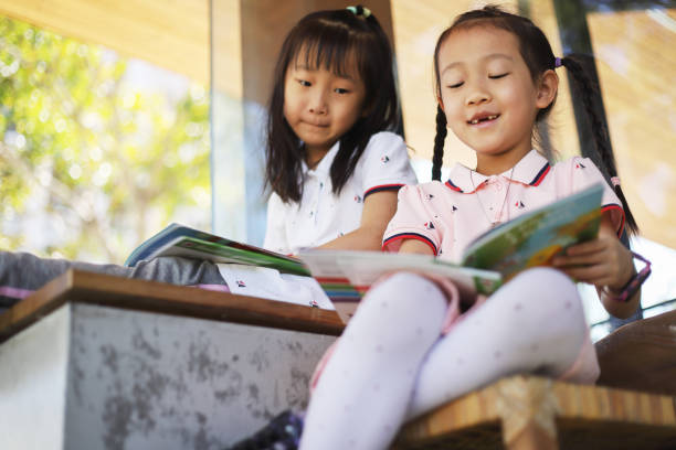 two smiling Asian girls reading a book outdoors.