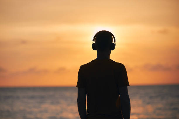 silueta del hombre con auriculares contra el océano - escape from it all audio fotografías e imágenes de stock