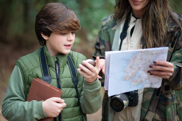 Focused boy and woman with cameras walking in forest Focused boy and woman with cameras walking in forest. Dark-haired mother and son in coats getting ready to take pictures, discussing route. Parenting, family, leisure concept orienteering stock pictures, royalty-free photos & images