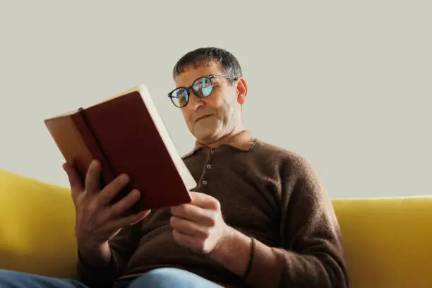 old man asian professor historian reading old book at home. old age, leisure and people concept, senior man sitting on sofa and reading book at home