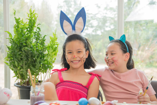 istock two cute little sisters wearing bunny ears playing egg hunt on easter. adorable children celebrate easter at home. Teenage asian girl painting and decorating Easter eggs. 1386898590