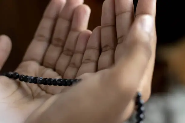 Young Muslim woman praying with Tasbeeh. The background is Blurry, Indoors. Focus on hands.
