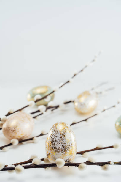 istock Blooming pussy willow branches and golden eggs in different patterns and colors on the white background. Minimalist, Modern vertical Happy easter card. Selective focus, copy space. 1386899277