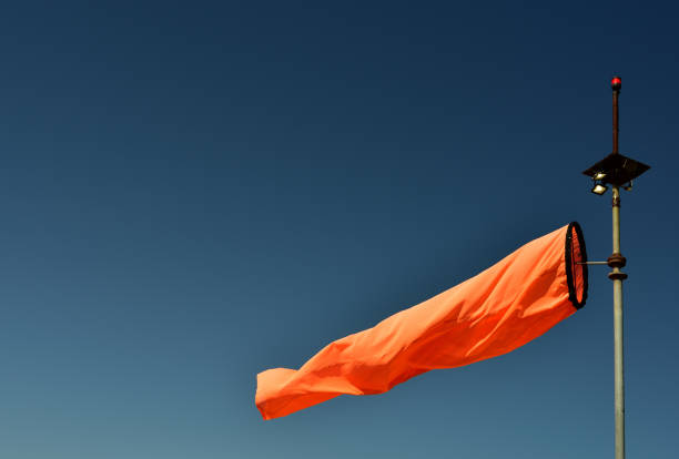 istock Bright neon orange wind sock blowing indicating wind direction against an azure sky 1386903681