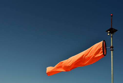 Bright neon orange wind sock blowing indicating wind direction against an azure sky