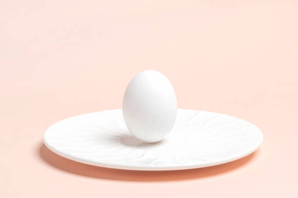 istock One white chicken egg is standing on white plate on pastel pink backdrop. Easter minimal image. 1386905287