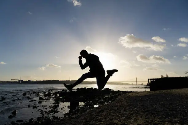 Photo of Silhouette of a man jumping on the bank of the Tagus River at sunset