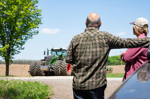 A farming couple looking at a tractor contemplating a decision