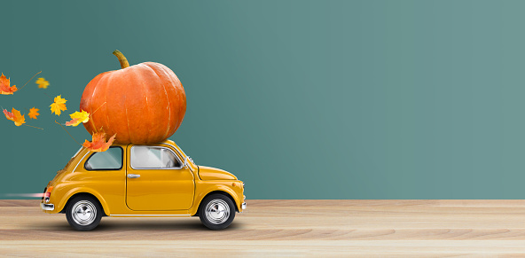 Thanksgiving is coming. Yellow retro car with big pumpkin on a roof.