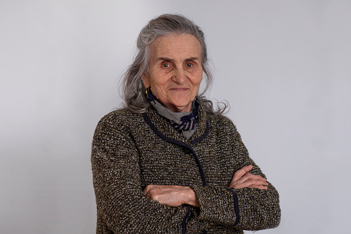 Senior woman arms crossed, looking directly in to the camera and smiling. White background with copy space.