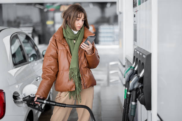 woman in face mask refueling car with a gasoline using smart phone - gas station gasoline refueling fuel pump imagens e fotografias de stock