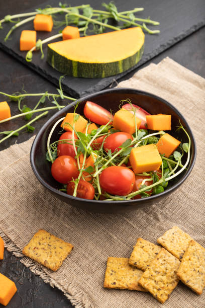 vegetarian vegetable salad of tomatoes, pumpkin, microgreen pea sprouts on black concrete background. side view. - portion pumpkin vegetable black imagens e fotografias de stock