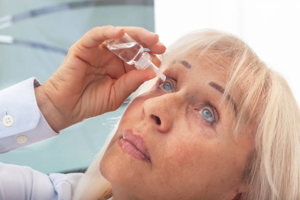 Senior woman drips eye drops into her eyes stock photo