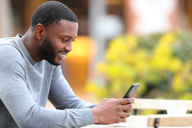 istock Happy man with black skin using phone in a coffee shop 1386921906