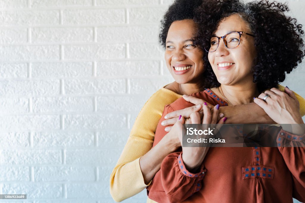 Gay couple hugging and looking away Portrait of two lesbian women hugging and looking away against white background Couple - Relationship Stock Photo
