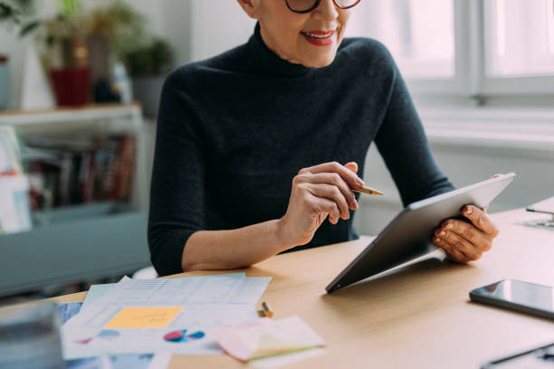 istock An Anonymous Beautiful Smiling Elegant Senior Woman Reading Something On Her Tablet While Sitting At Her Desk In The Office And Working 1386923734