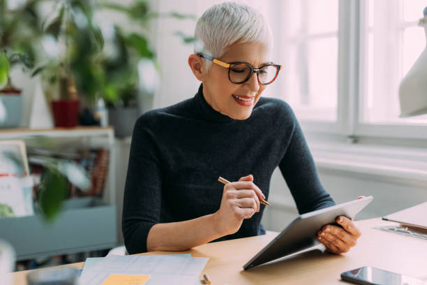 istock A Beautiful Smiling Elegant Senior Woman Reading Something On Her Tablet While Sitting At Her Desk In The Office And Working 1386923736