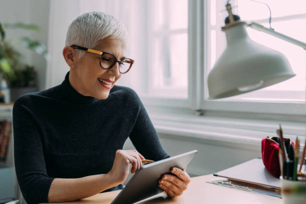 istock A Beautiful Smiling Elegant Senior Woman Reading Something On Her Tablet While Sitting At Her Desk In The Office And Working 1386923768
