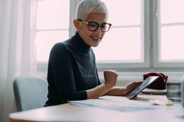istock A Beautiful Smiling Elegant Senior Woman Holding Her Tablet And Looking At Some Notes While Sitting In Her Office And Working 1386923806