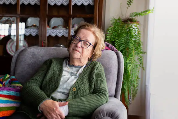 82 year old woman wearing green, sitting by the window in the sofa, portrait