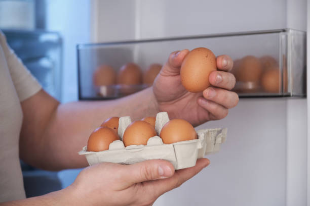 Close up of a man placing eggs in the fridge door shelf. stock photo