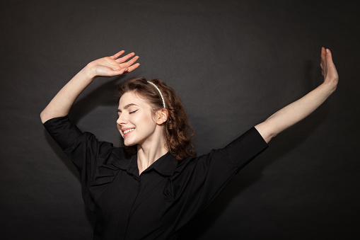 Studio portrait of a 20 year old woman with curly brown hair in a black shirt on a black background