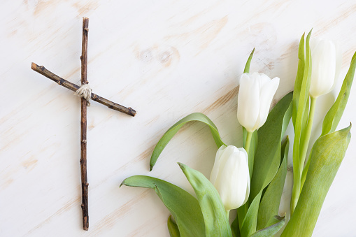 White tulips and a simple Christian cross on a white wood background shot from above