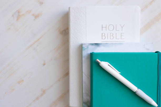 Stack of books with bible and teal journal on white