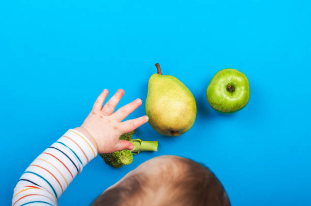 Child reaches out with his hand for pear and apple on blue background. Baby food, first feeding. . Child reaches out with his hand for pear and apple on blue background. Baby food, first feeding. food allergies stock pictures, royalty-free photos & images