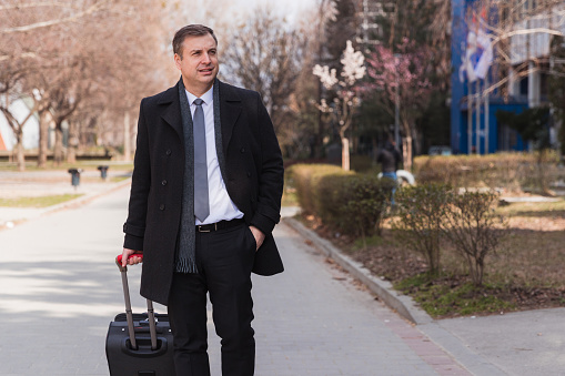 Man wearing a suit frowning and concentrating when pulling a suitcase and looking for a hotel where he is at during business travel